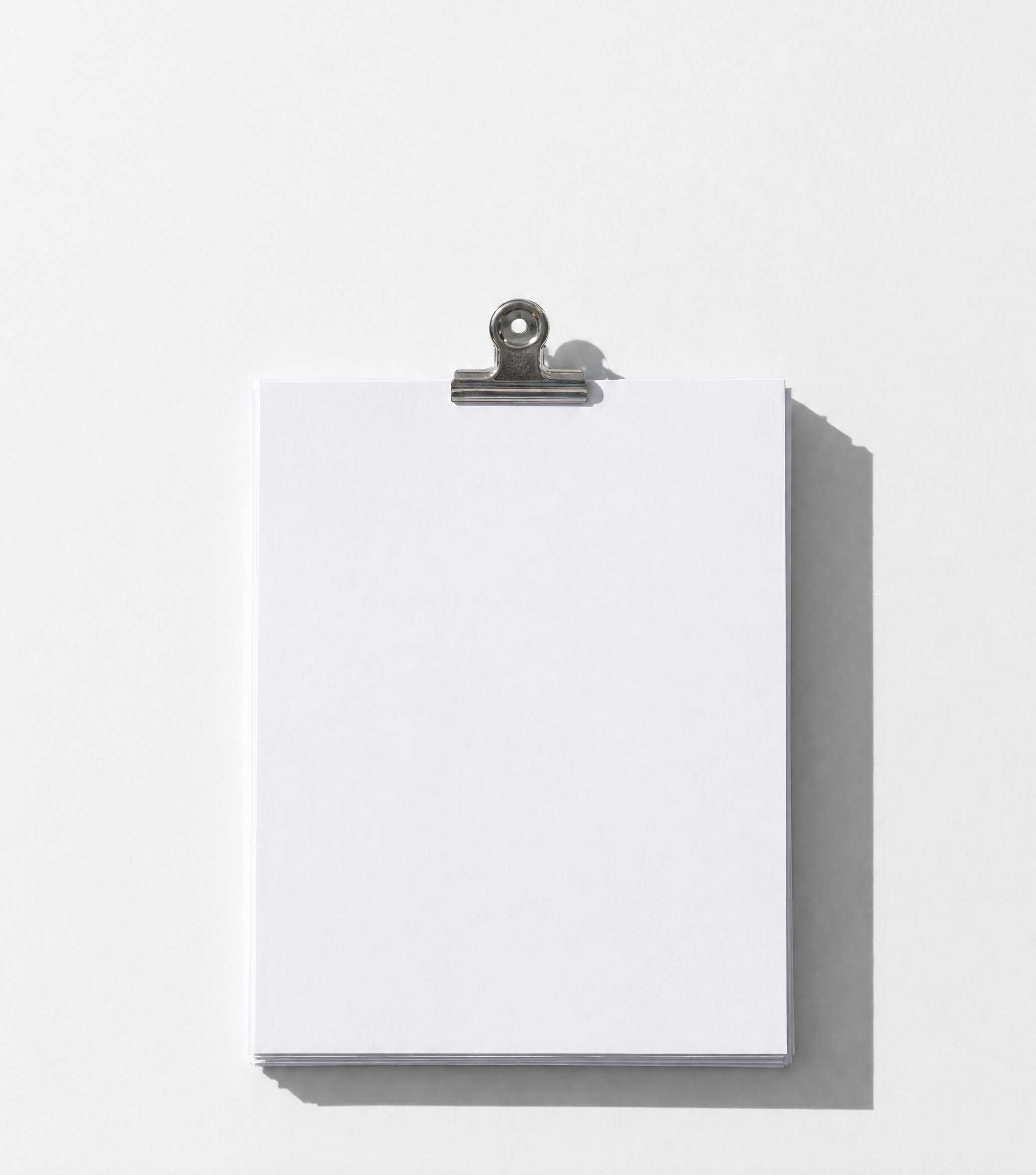 A squared stack of blank white invoices held by one steel bulldog clip, casting a long shadow.