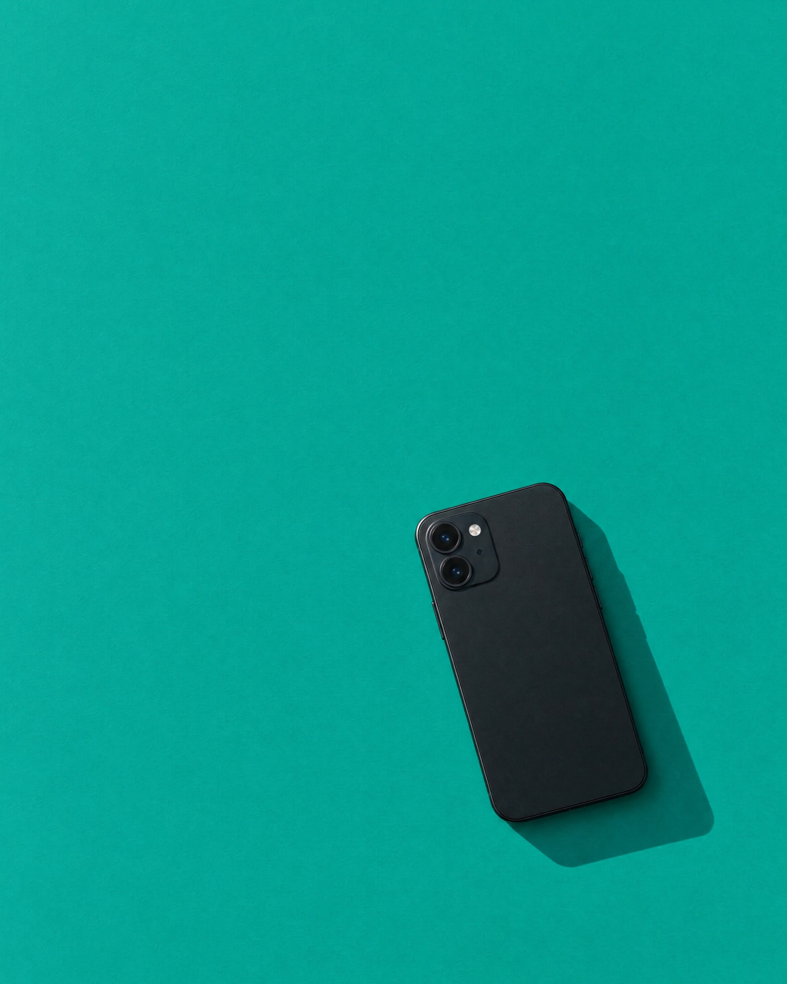A phone lying face down on a flat teal surface in hard sunlight.
